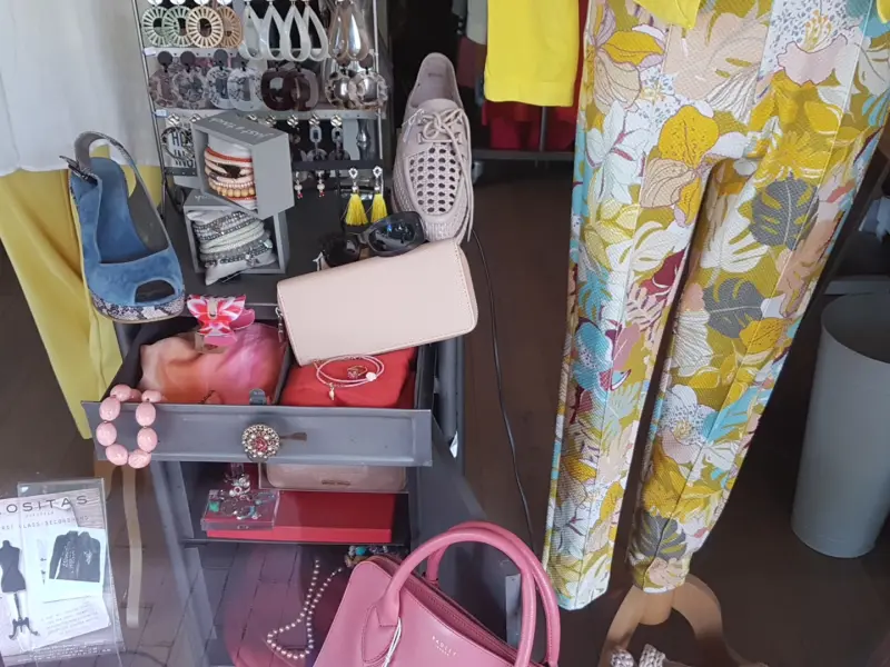In de etalage: een roze handtas, sieraden, oorbellen, schoenen en een broek met bloemenprint